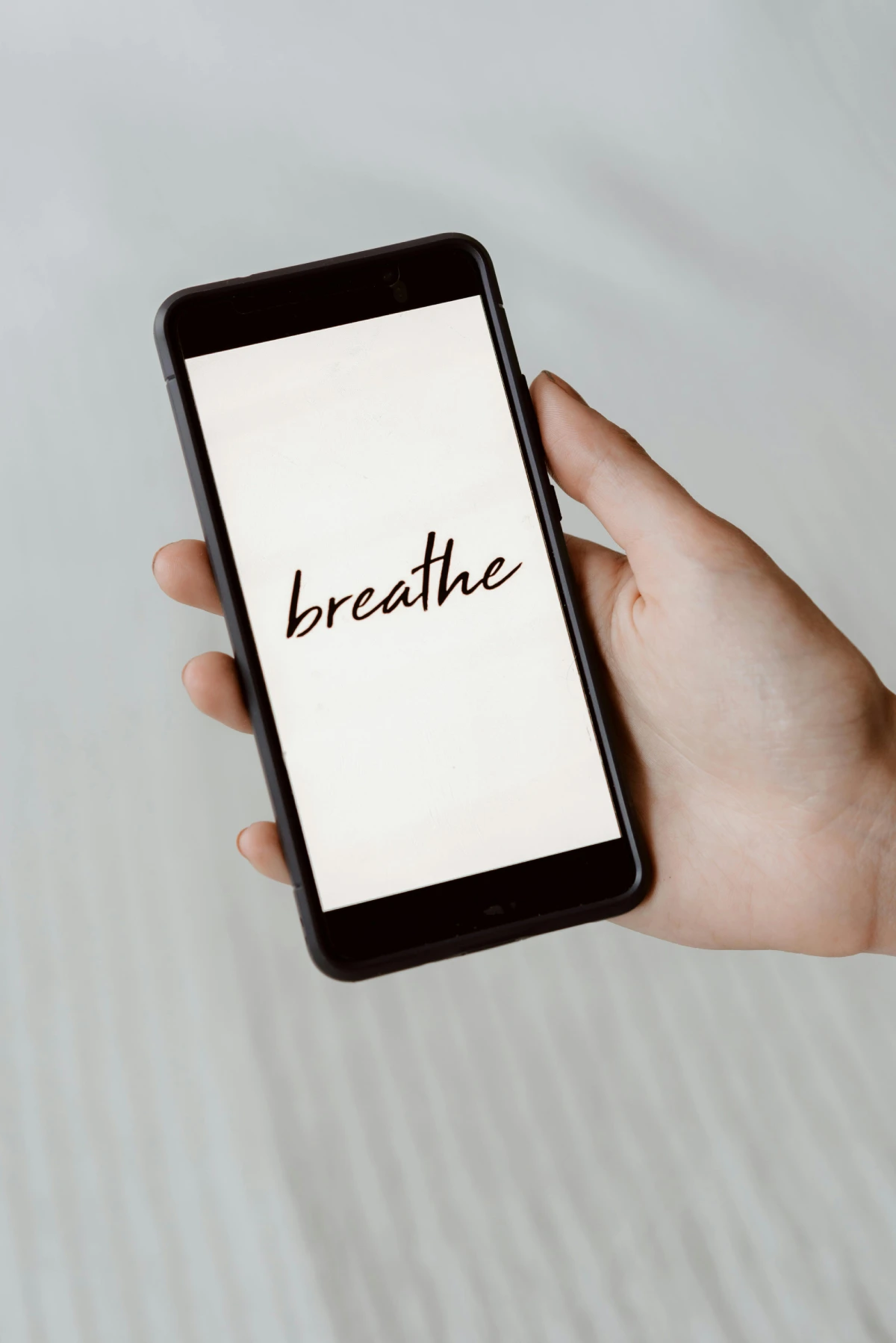 Mano sujetando un móvil con la palabra “breathe” en pantalla, invitando a practicar técnicas de respiración