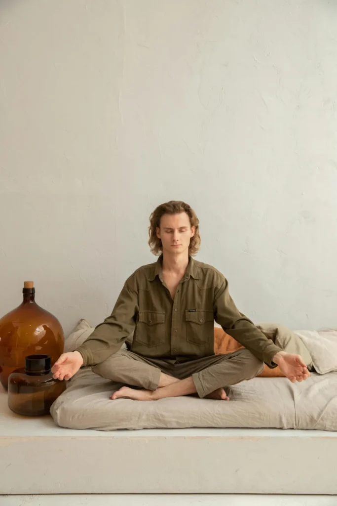 Hombre sentado en postura de meditación en casa, con los ojos cerrados y respiración consciente.